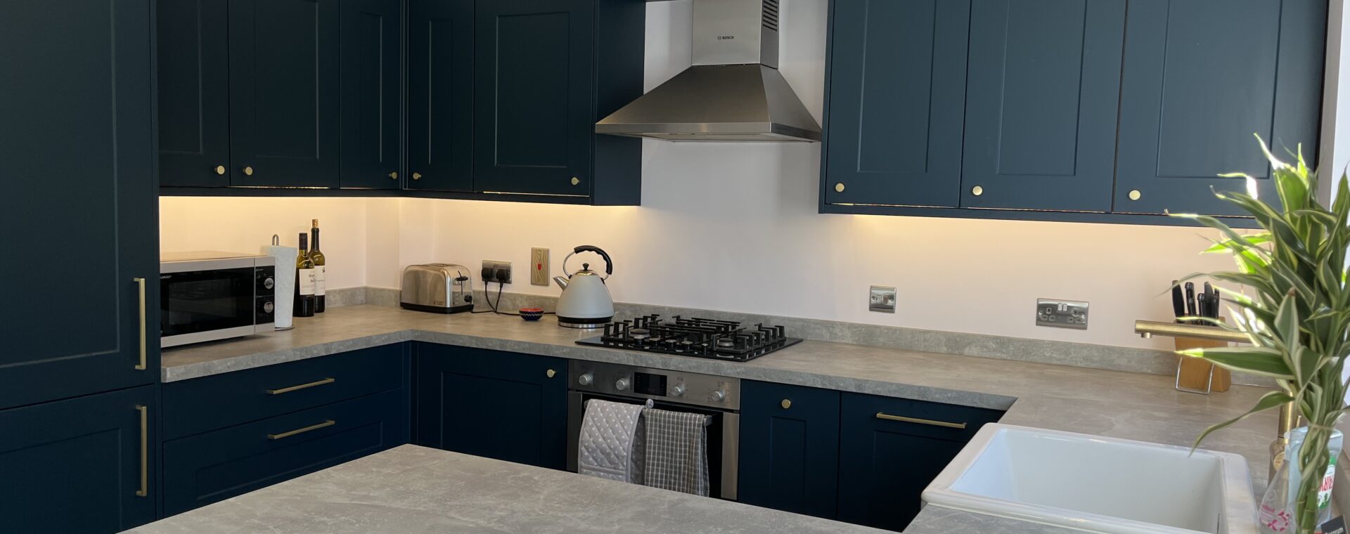 Navy blue shaker kitchen with brass hardware, concrete-look worktops, gas hob and stainless steel chimney extractor