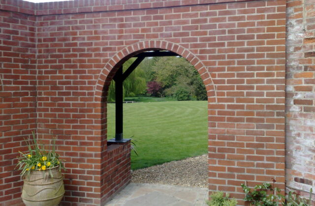 Close view of a brick archway with a soldier-course arch ring, looking through to a lawn