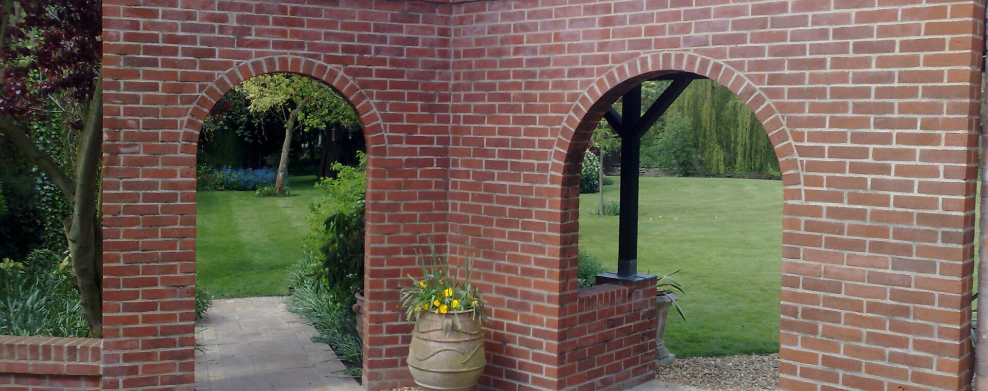 Red brick garden wall with two semicircular arches opening onto a lawn