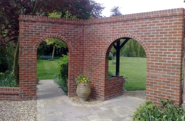 Red brick garden wall with two semicircular arches opening onto a lawn