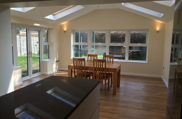 Single-storey extension in Cambridge with a dual-pitched vaulted ceiling, Velux roof windows, a central island and oak-effect flooring