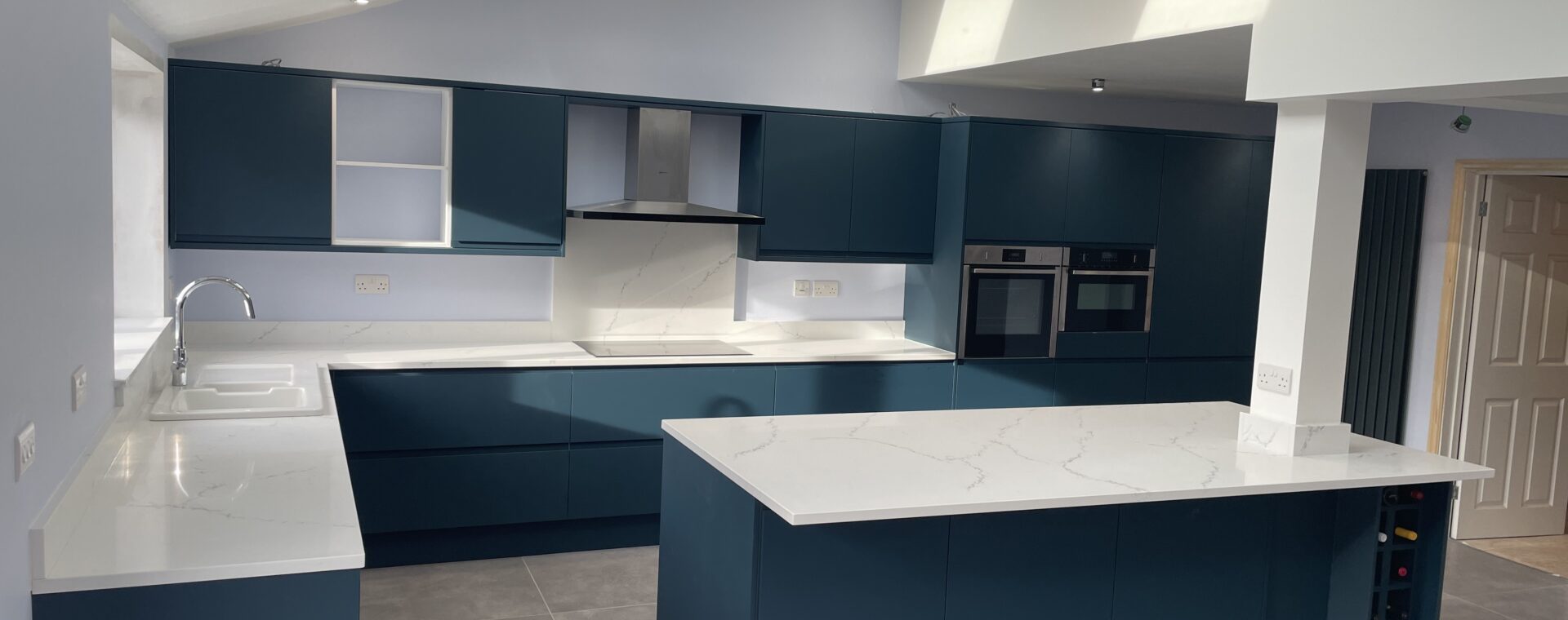 Open-plan kitchen in a single-storey lean-to extension in Cherry Hinton, Cambridge, with a vaulted ceiling, Velux skylights and dark teal handleless units
