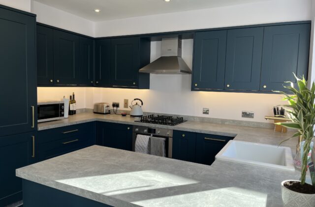 Navy blue shaker kitchen with brass hardware, concrete-look worktops, gas hob and stainless steel chimney extractor
