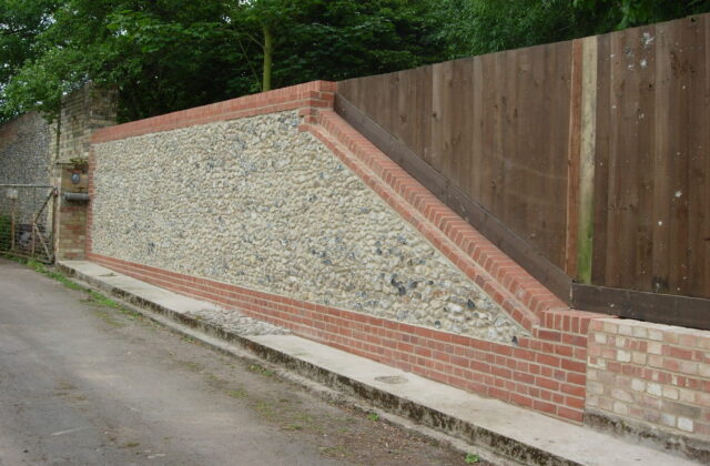 Flint panel framed by red brickwork, ramped to follow the fall of the lane