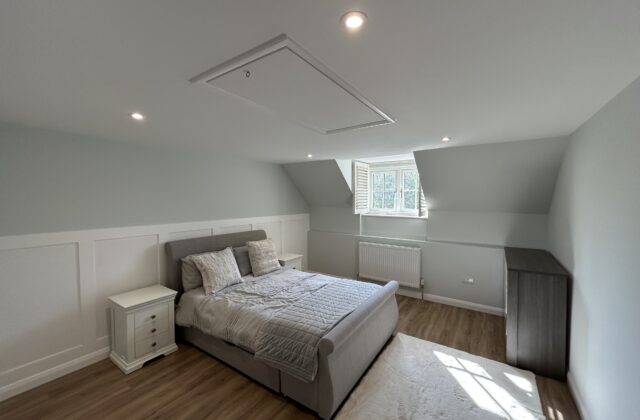 Newmarket bedroom refurbishment with custom white accent wall panelling, sage green walls, LVT flooring and internal window shutters