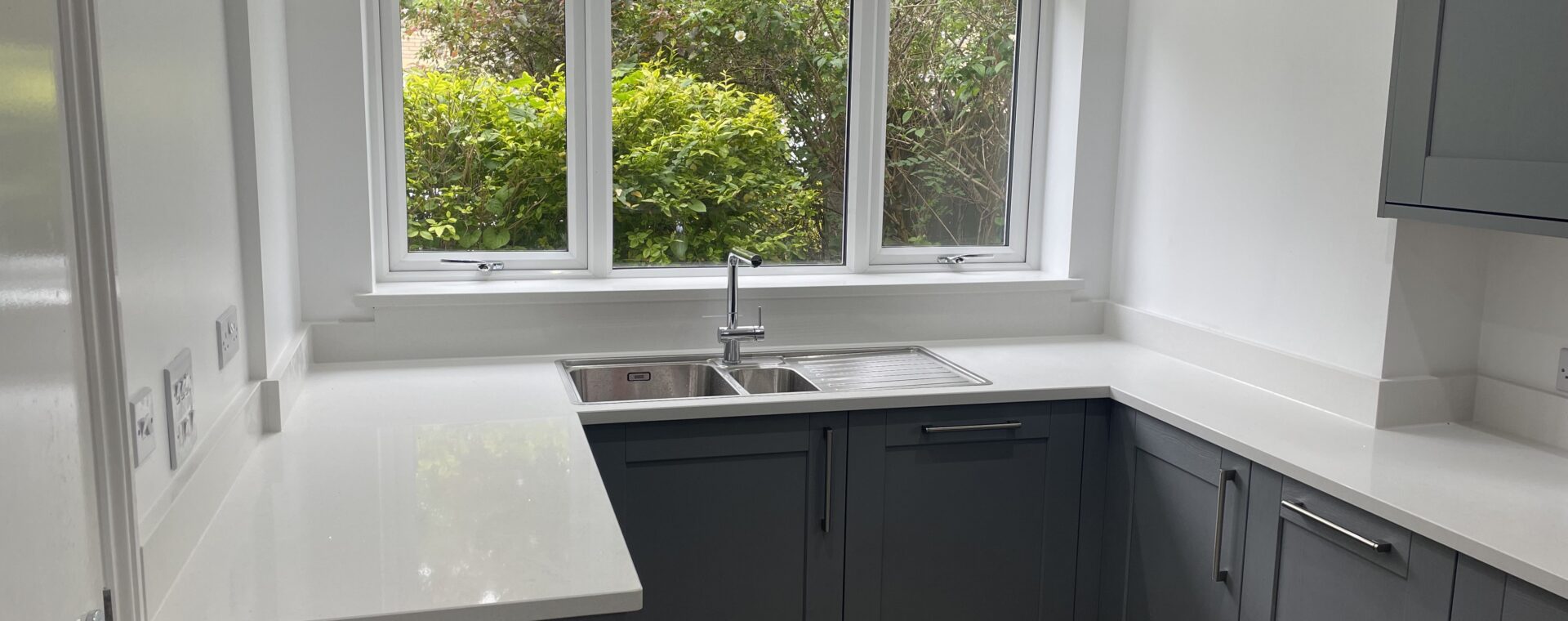 U-shaped slate-grey shaker kitchen in a bay window extension with white quartz worktops and a stainless steel sink and drainer