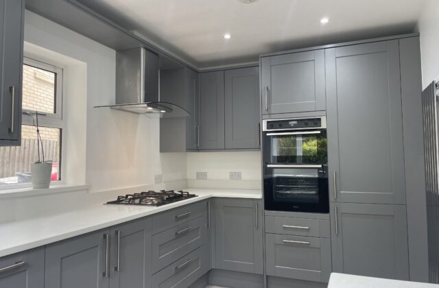 Slate-grey shaker kitchen with gas hob, chimney extractor and built-in double oven above herringbone vinyl flooring