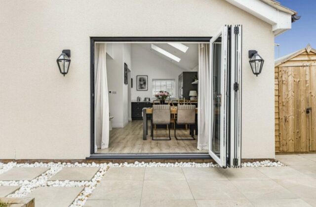 Rear elevation of the Waterbeach extension with aluminium bifold doors opened onto a porcelain patio, looking through to the dining space