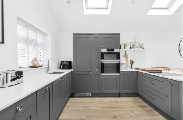 U-shaped dark grey shaker kitchen with white worktops, integrated double oven and a window above the sink in the Waterbeach extension